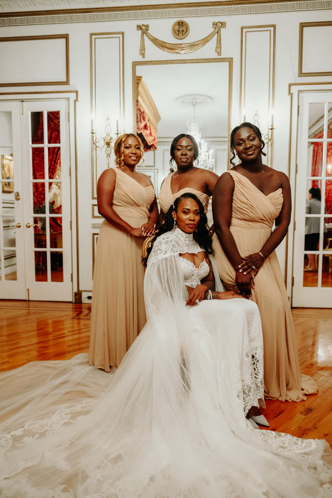 Bride wearing Calla Blanche Wedding Gown and Cape poses with Bridesmaids at James Ward Mansion Wedding