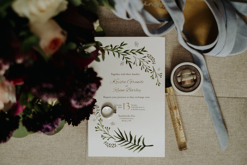 Flatlay of wedding invitation, wedding bands and bride's details