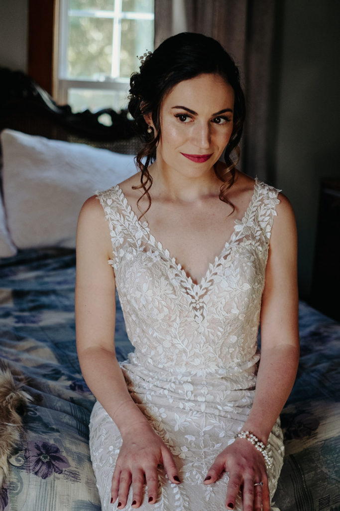 Bride wearing BHLDN wedding gown sits on the edge of bed for portrait