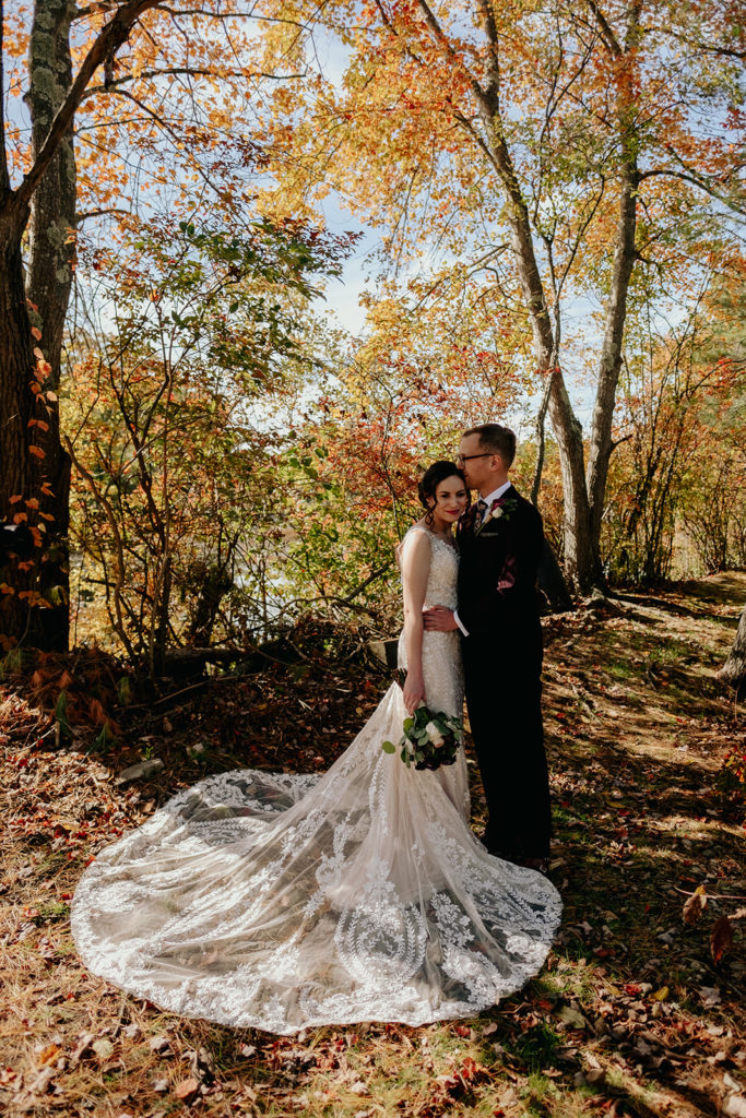Bride wearing BHLDN and Groom wearing Incodchino Tux pose for portrait in fall foliage