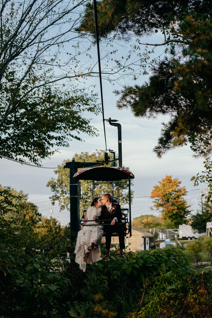 Bride wearing BHLD wedding Gown and groom wearing Indochino suit kiss while on the sky safari chairlift at Southwick's Zoo Mendon MA