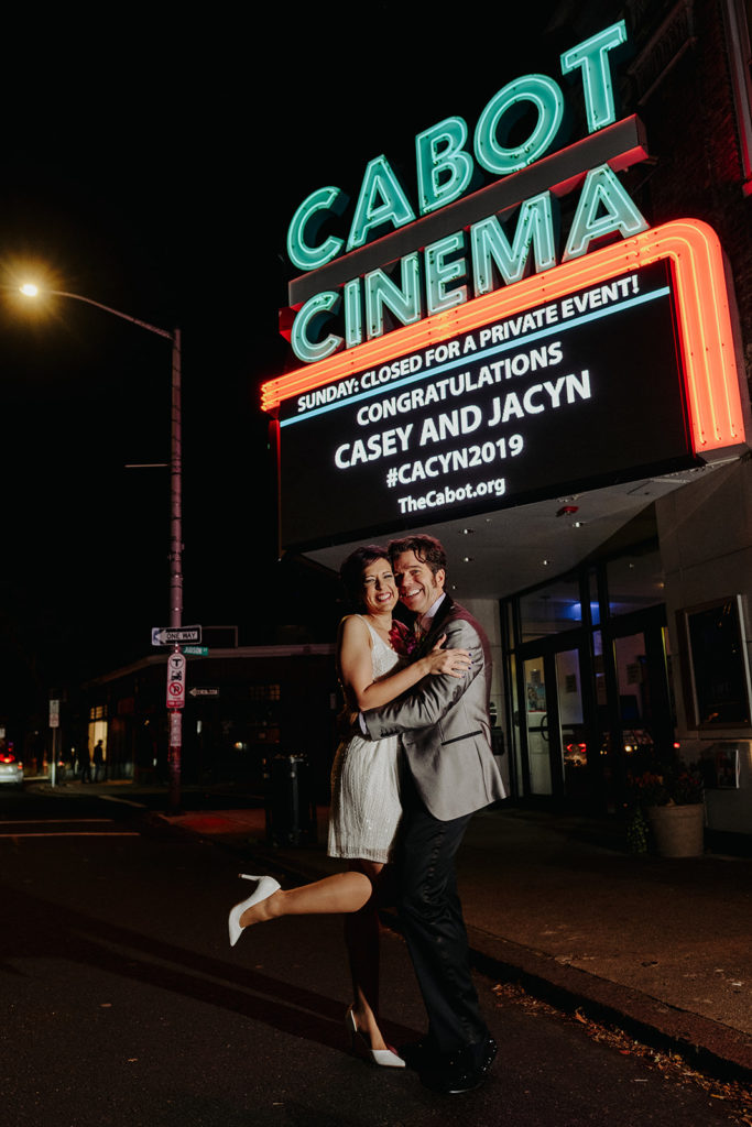 Bride and groom pose with the cabot Cinema Marquee at their wedding at night