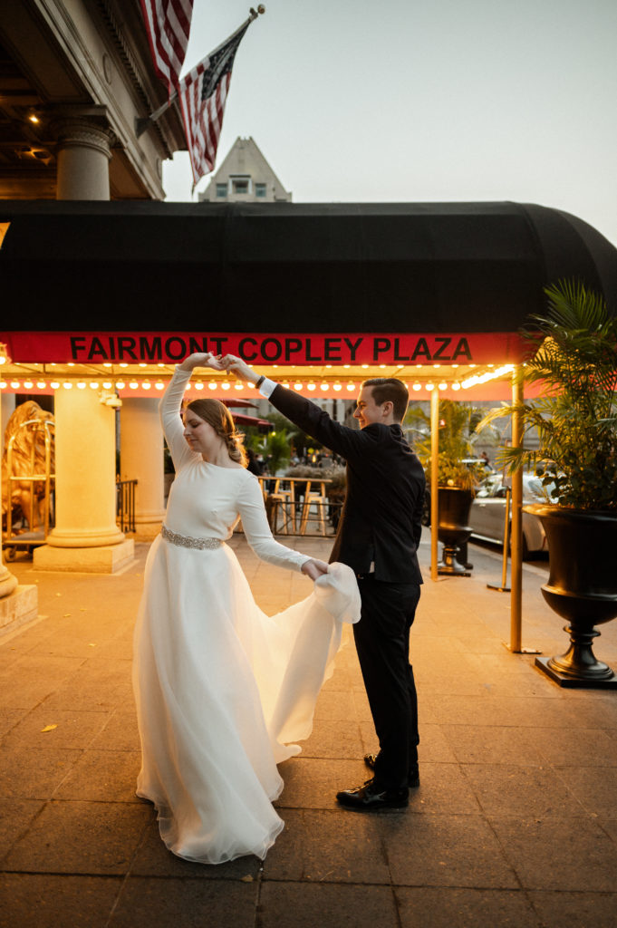 Groom twirls bride wearing a BHLDN gown infront of the Fairmont Copley Plaza Boston