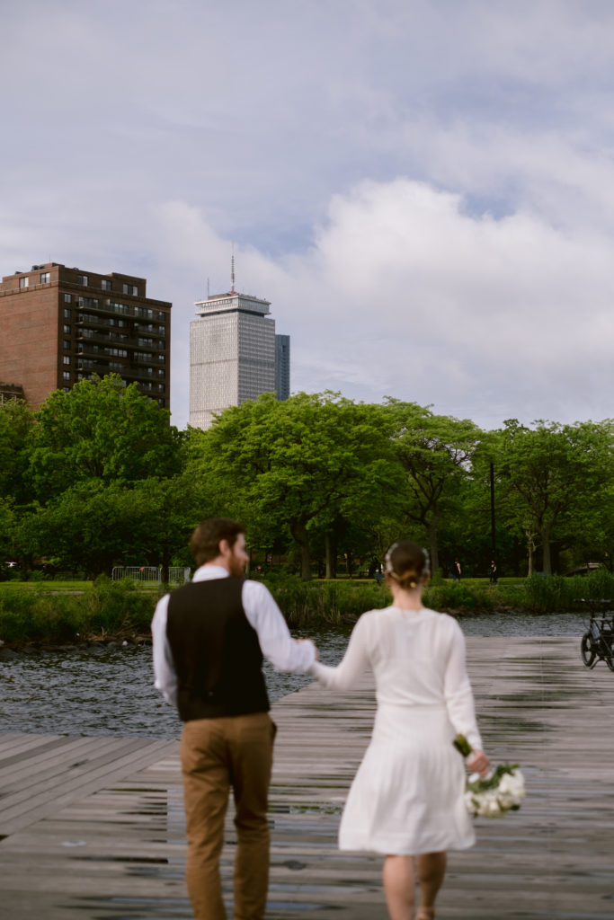Bride and groom walk along dock of the Charles River as the Boston Prudential Building is in the background