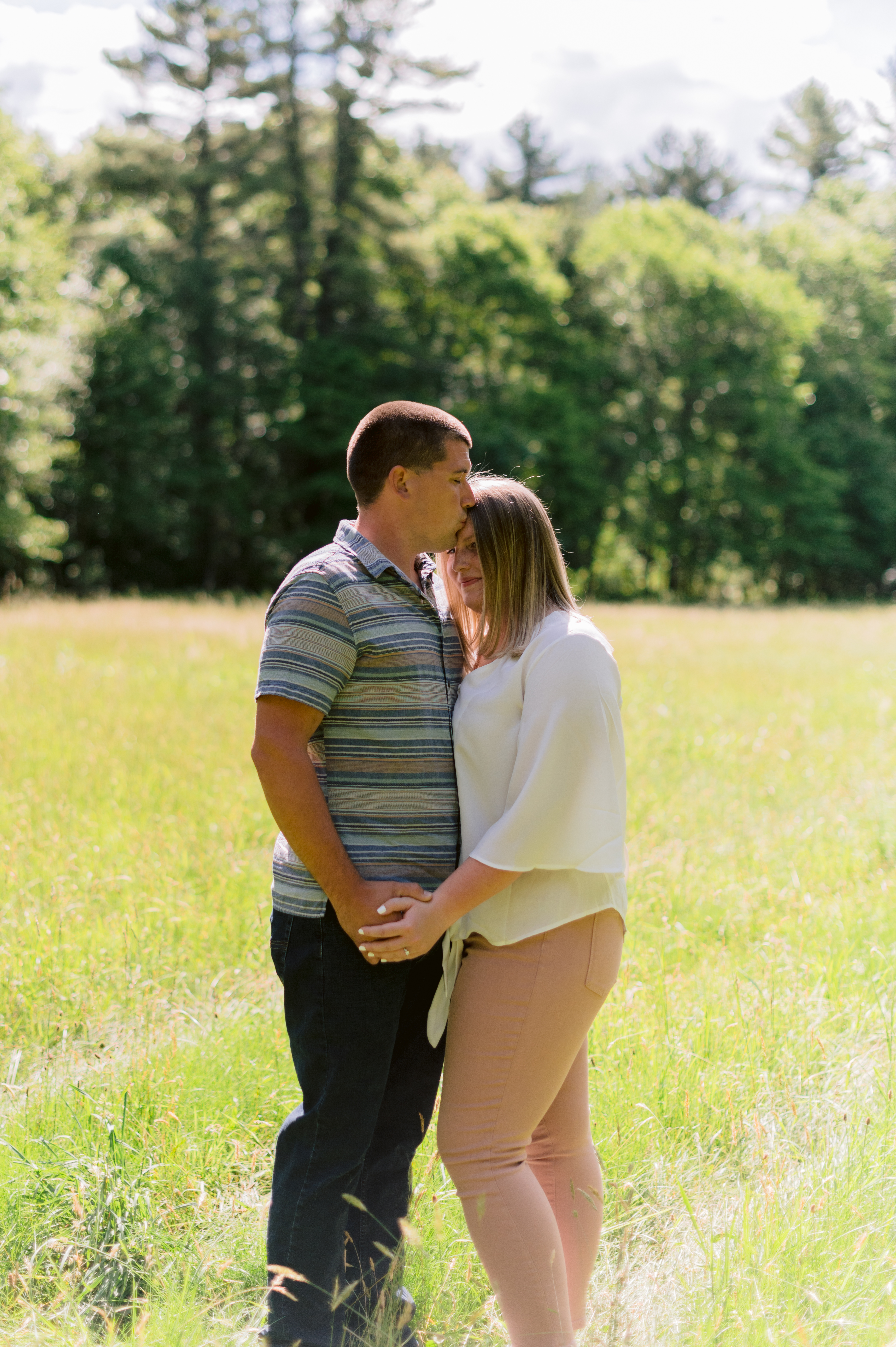 Man kisses woman on the forehead in field during summer engagement session at Borderland State Park