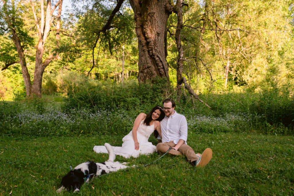 Bride and groom sit in grass with their dog during Berkshires Elopement