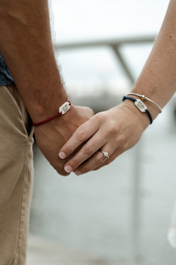 Couple holds hands and wears matching bracelets with wedding date during change the date session