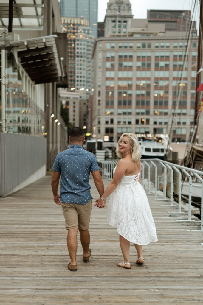 Couple walks together along Boston Waterfront by New England Aquarium boston seaport engagement session
