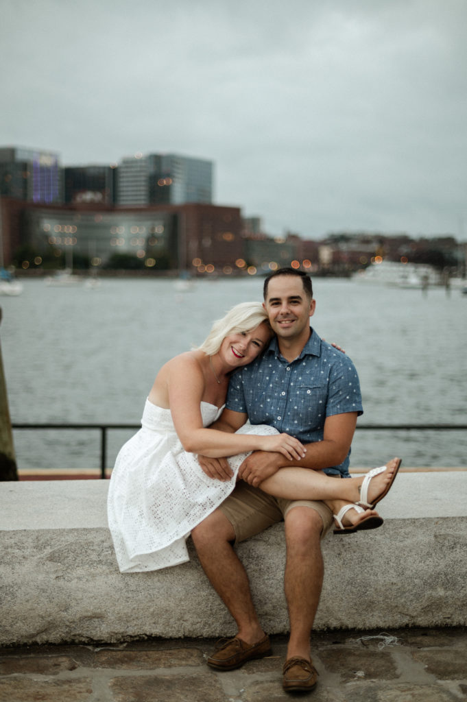 couple sit along Boston Harbor on Long Wharf Boston Engagement Session