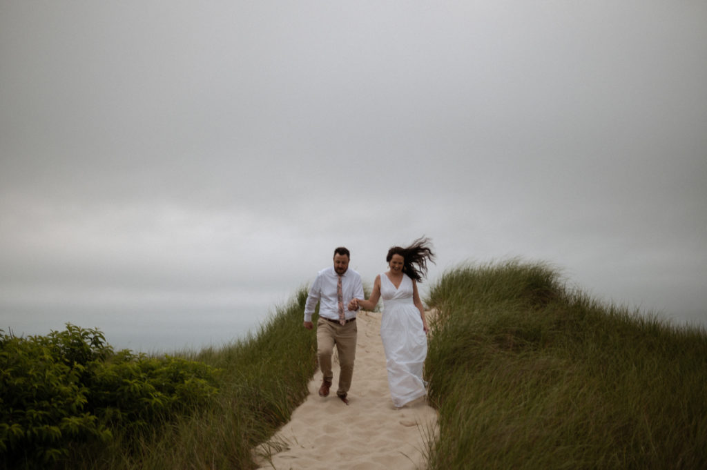 Bride and groom running in sand dunes at Crosby Landing Beach in Cape Cod Massachusetts Minimony Elopement