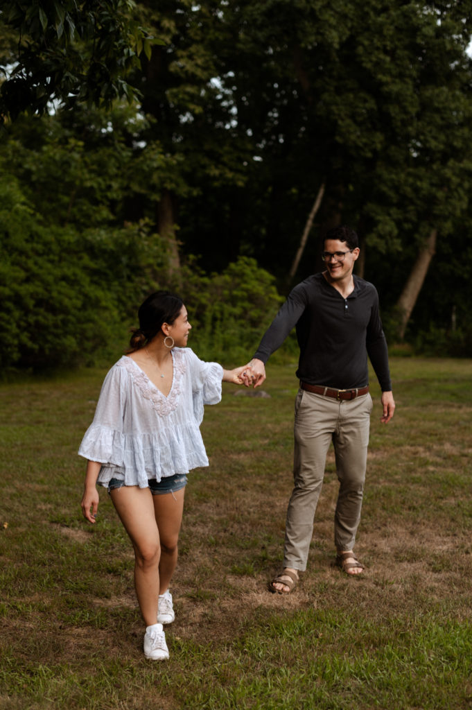 Couple holds hands and walks together during Engagement Session at Stonehurst Estate in Waltham