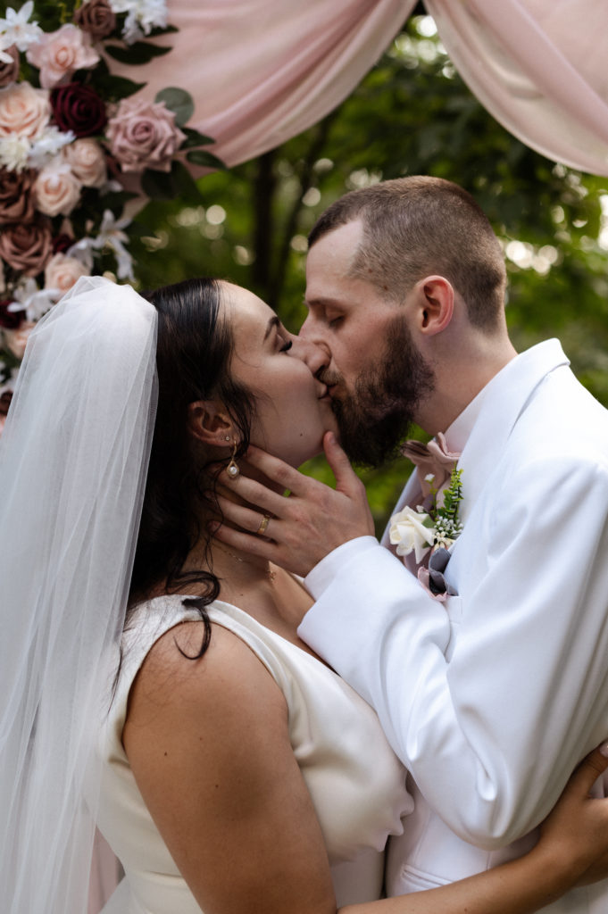 Bride and groom kiss under floral archway at New Hampshire White Mountains Wedding Elopement