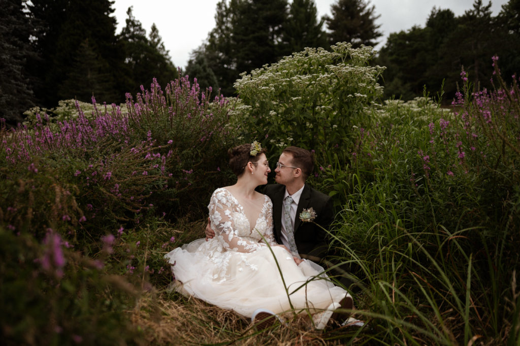 Bride and groom sit in wildflowers in Arnold arboretum during COVID 19 Elopement in Boston