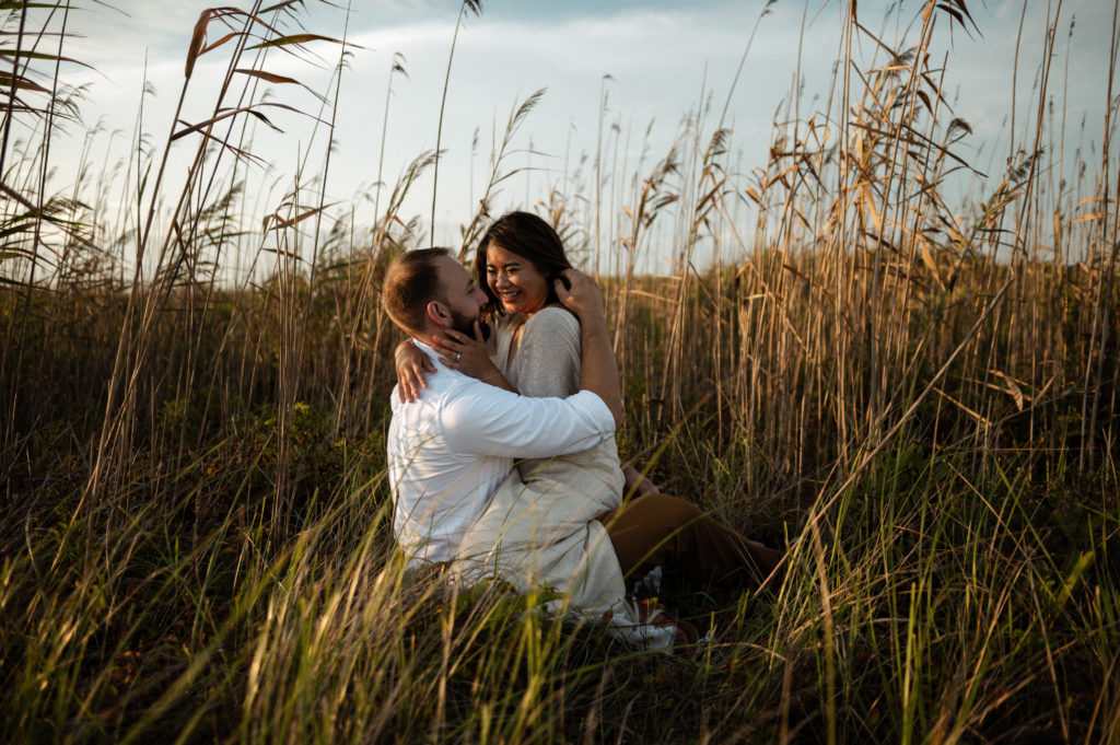 Man and woman hug in the grass by the beach on Gooseberry Island in Westport Massachusetts