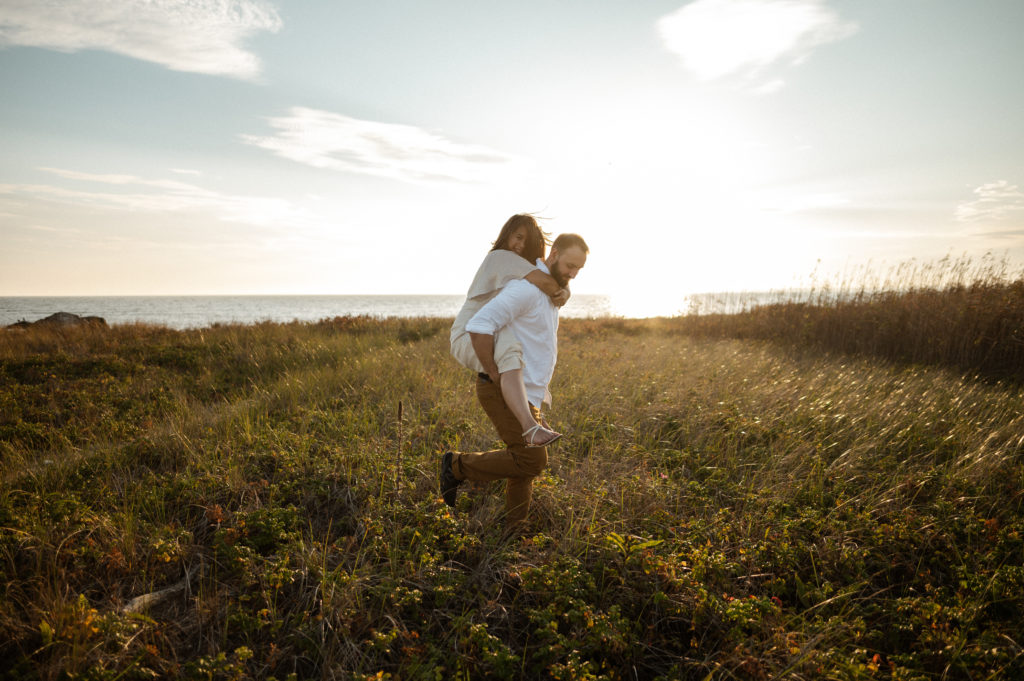 Man carries woman through grass during couples' session in Massachusetts on Gooseberry Island