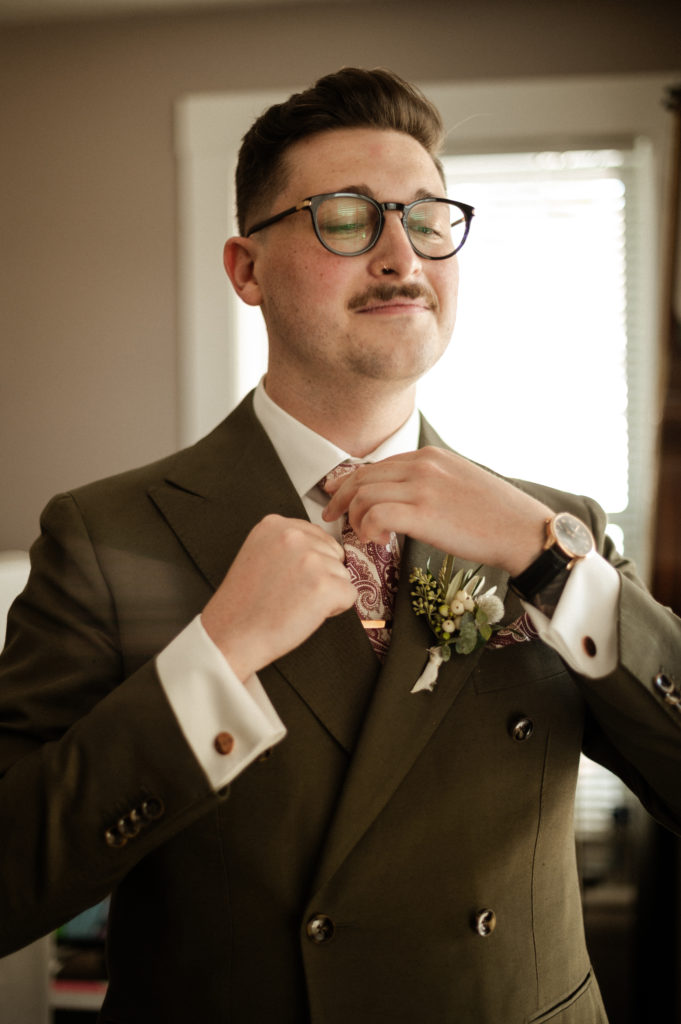 Glasses wearing groom wearing green double breasted suit with succulent details