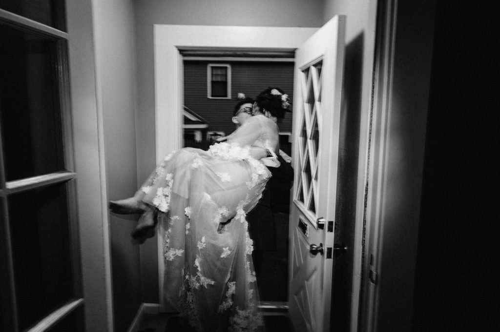 Groom carrying a barefoot bride in BHLDN gown through the door after getting married