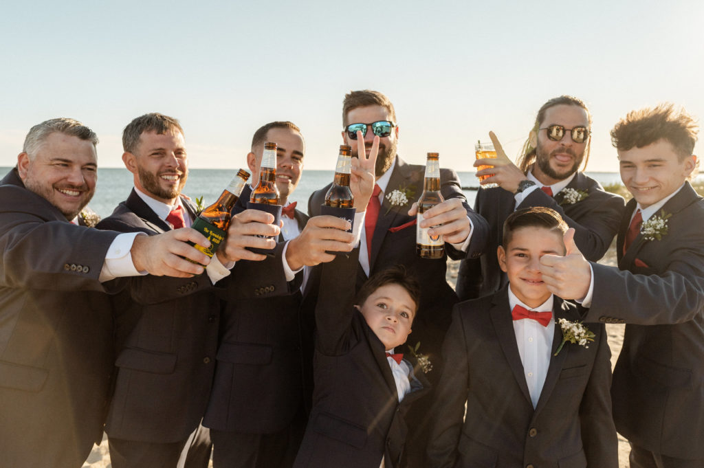 Groomsmen in navy suits with red bowties sharing a drink together at Cape Cod Wedding