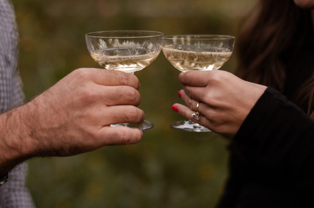 Close up of champagne in vintage glasses with engagement ring during engagement session