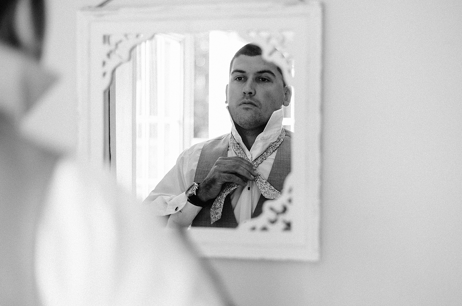 B&W Groom buttoning up shirt in mirror
