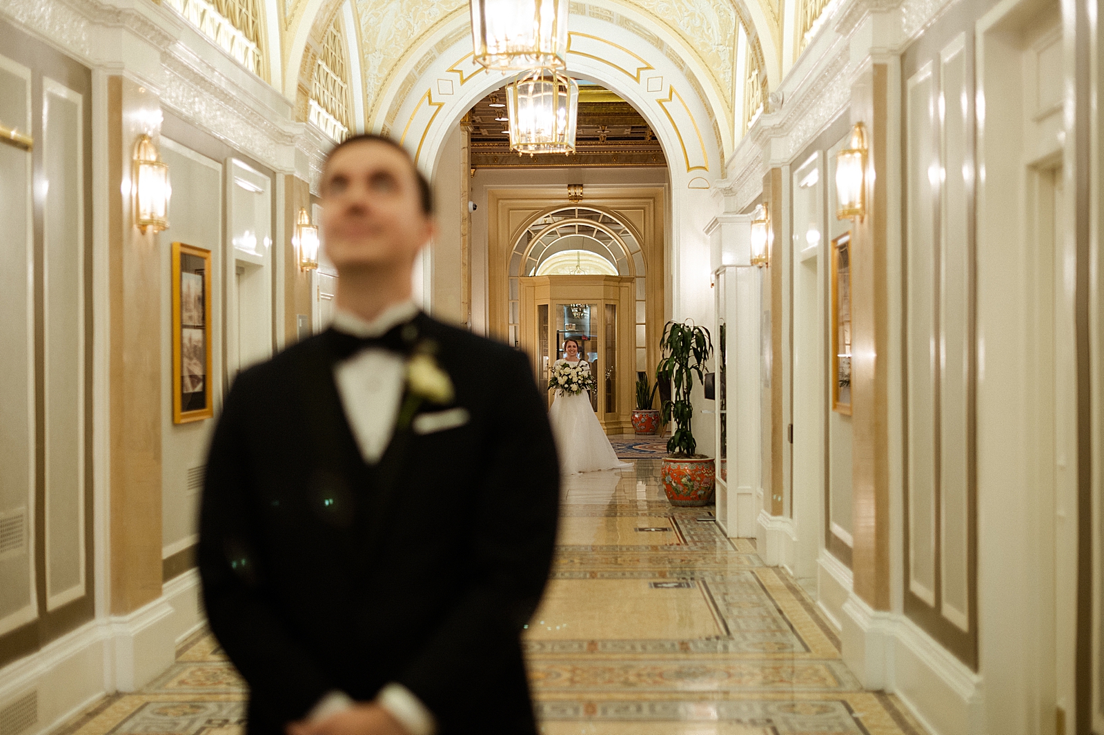 Bride approaching Groom in Ballroom hallway with bouquet