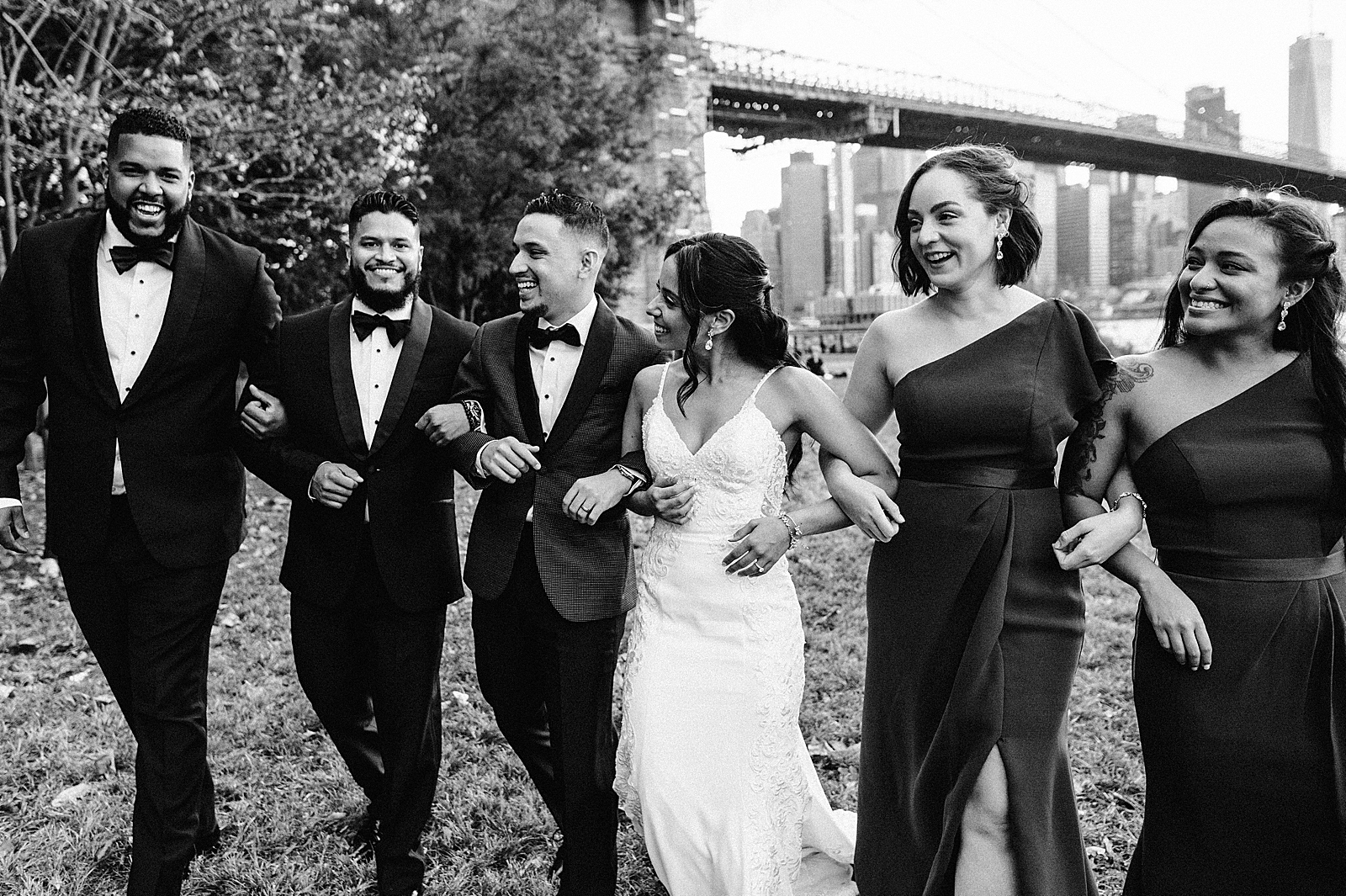 B&W Bride and Groom arm in arm with wedding party smiling