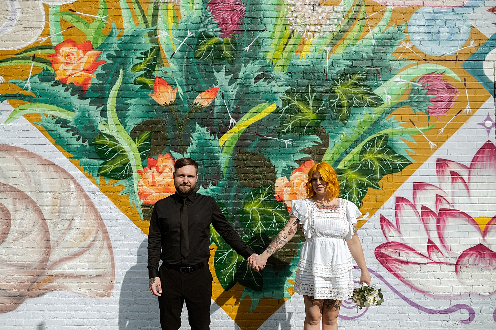 Bride and Groom extending their arms to hold hands in front of street art wall