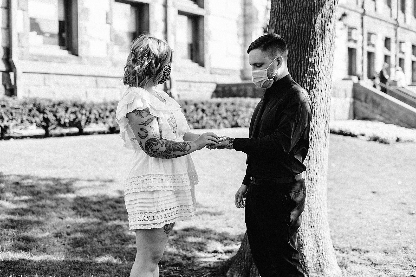 B&W Bride putting ring on Groom by tree