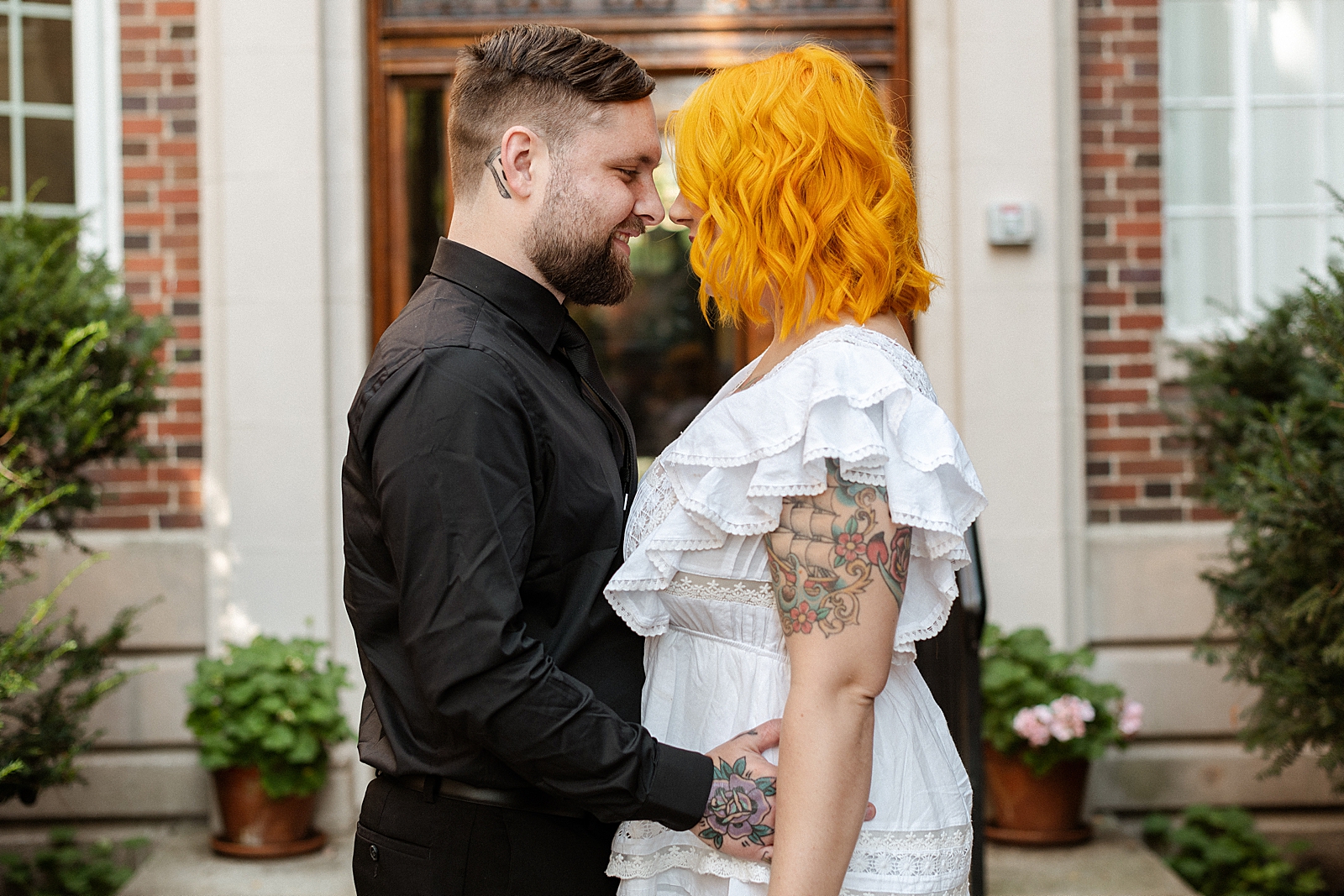 Groom holding Bride close face to face in front of brick building