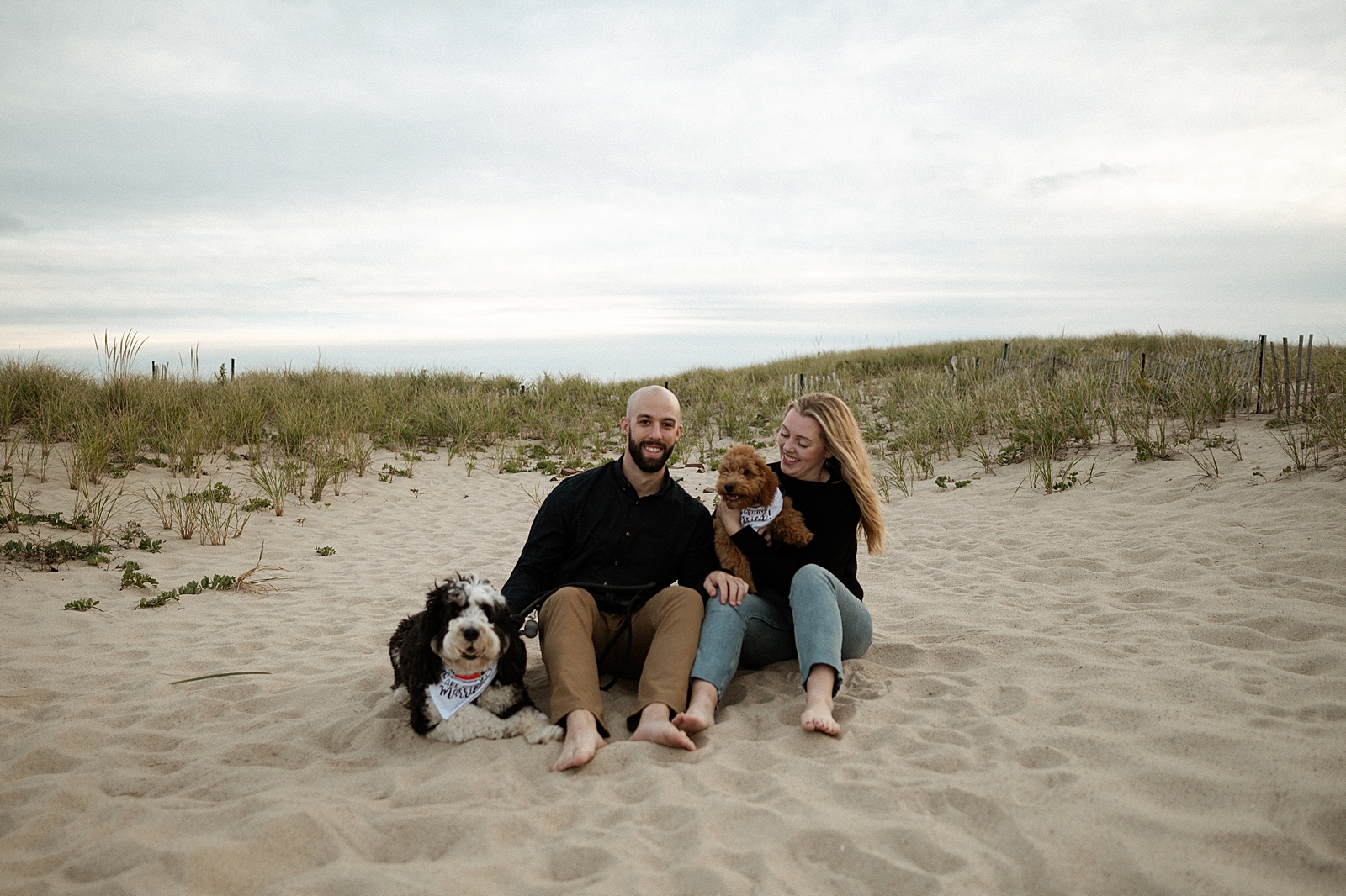 Couple sitting on the sand together with their dogs
