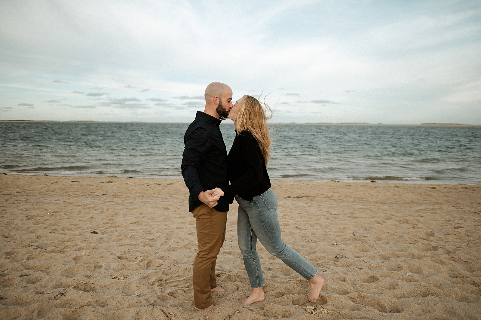 Couple kissing while standing on the sand in front of the ocean