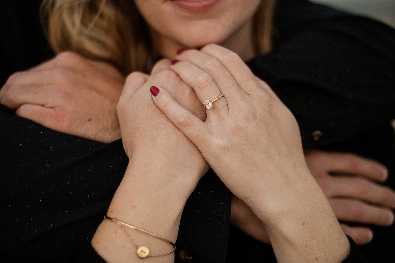 Closeup of man's arms wrapped around woman and showing off engagement ring