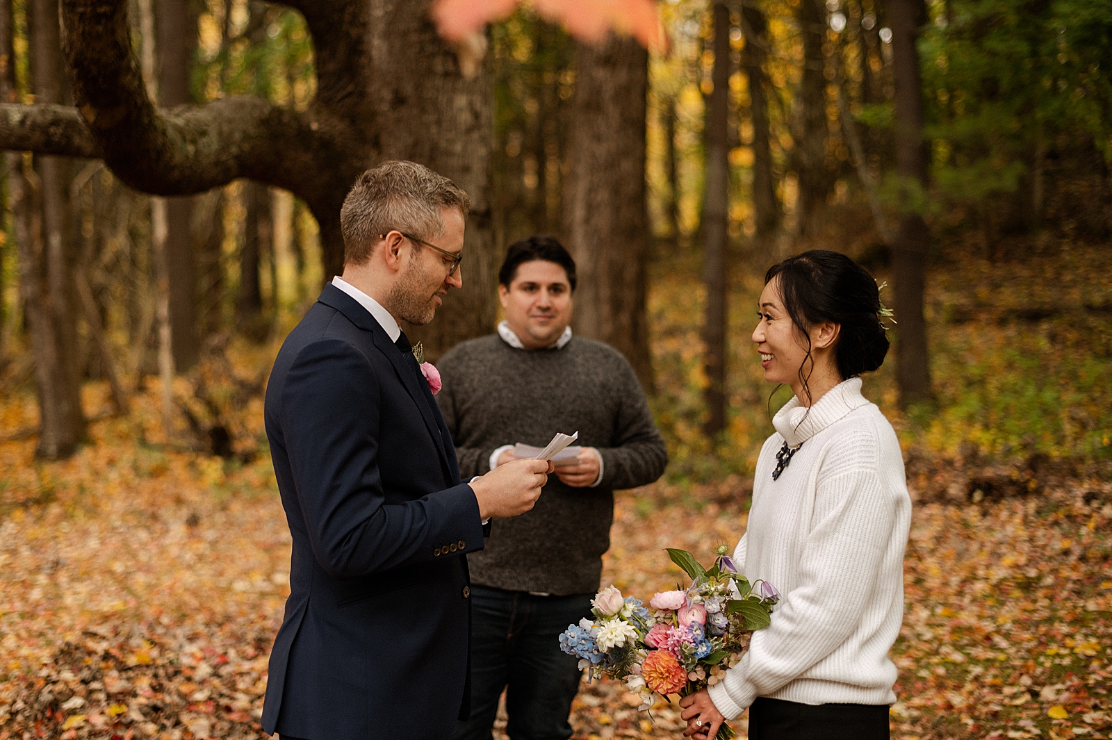 Groom reading vows to Bride while standing on autumn leaf ground