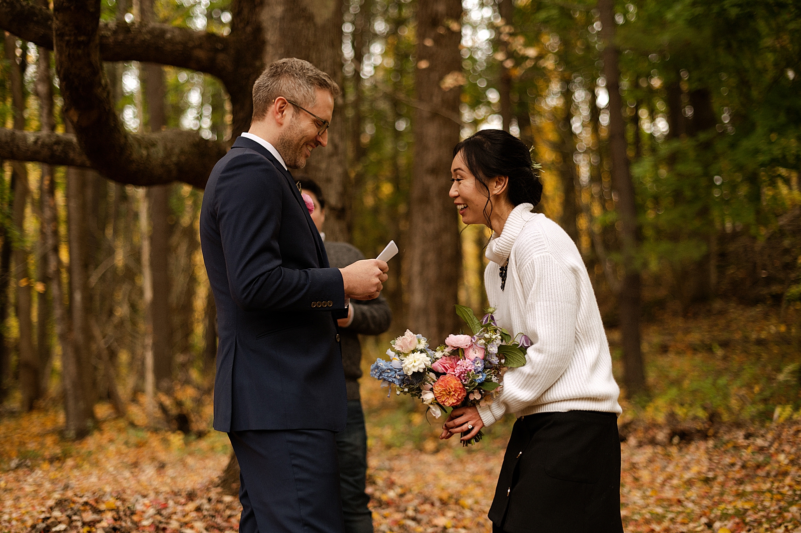 Bride laughing while Groom reading vows in fall forest