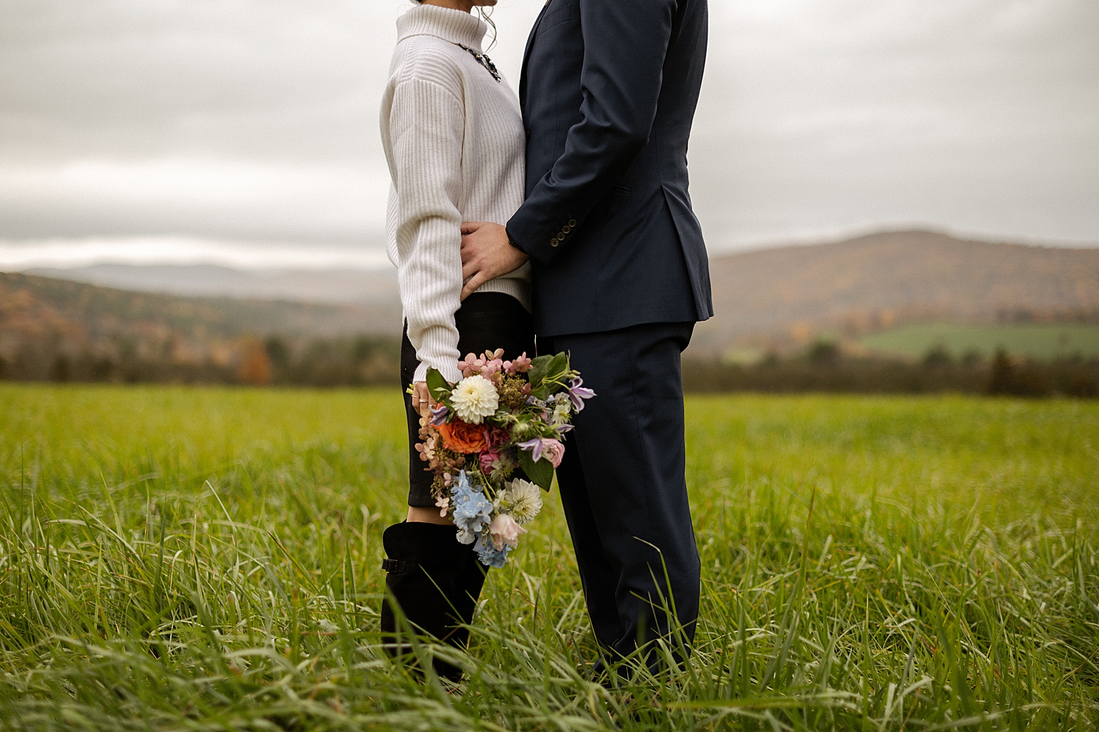 Closeup of Groom holding Bride and Bride holding bouquet in tall grassy field