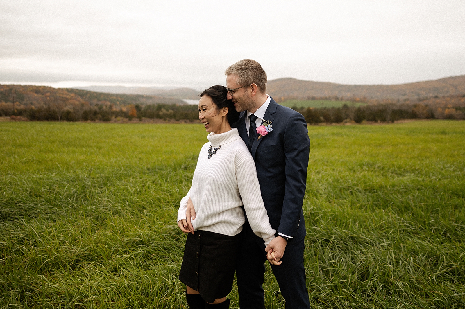 Groom holding Bride's hand from behind on grassy field
