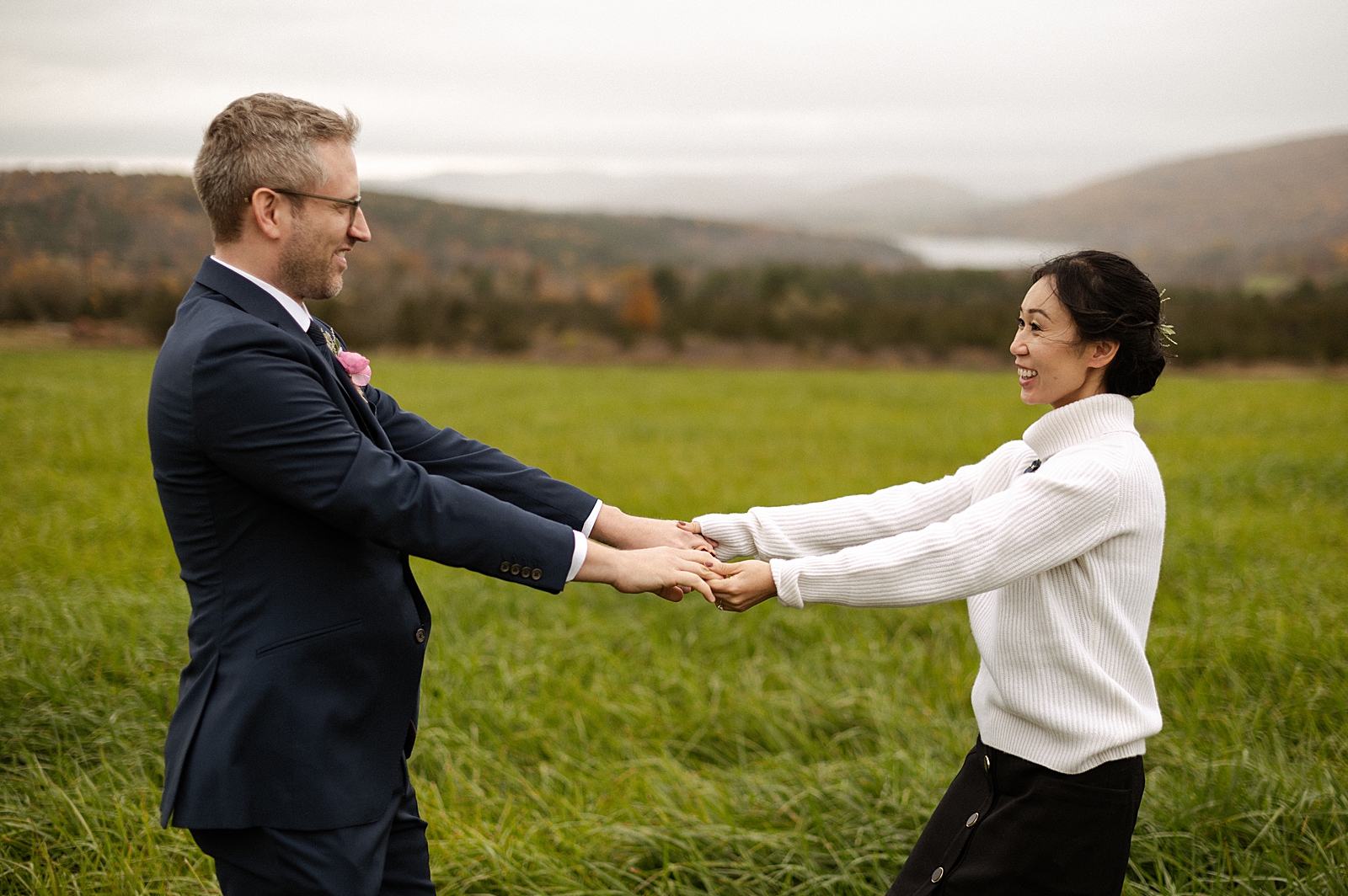 Bride and Groom extending their arms out and holding hands and twirling on tall grassy field