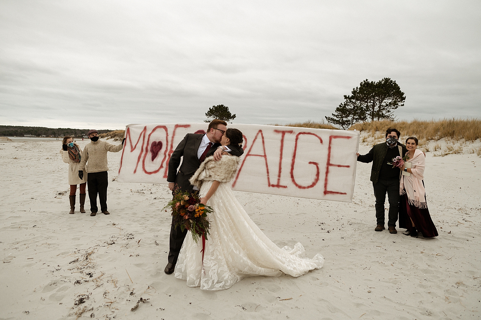 Bride and Groom kissing in front of Bride and Groom sign on the beach