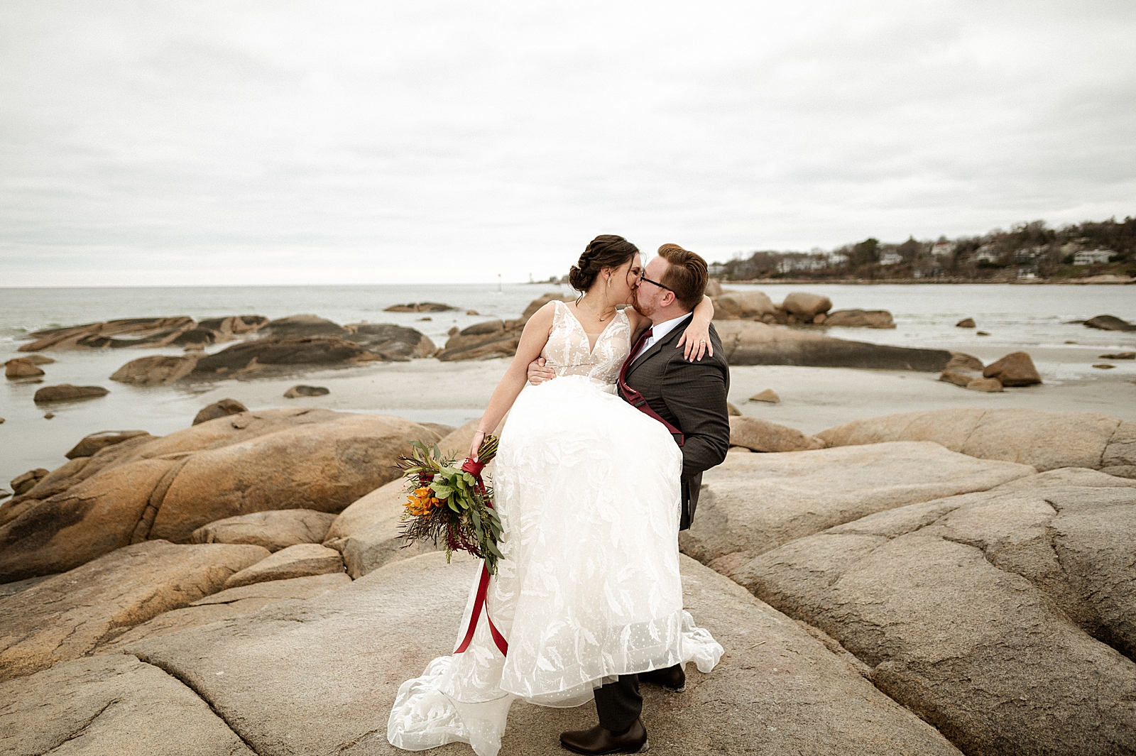 Groom holding Bride and kissing her on the rocky beach