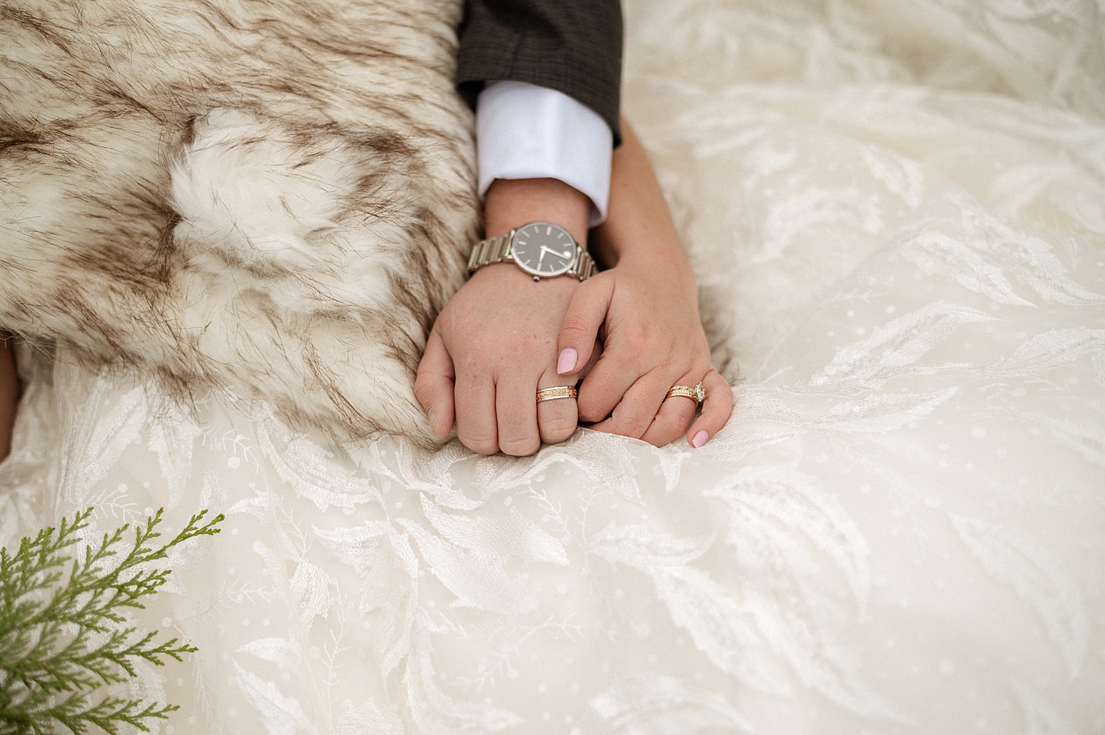Closeup of Bride and Groom holding hands with wedding bands on on wedding dress